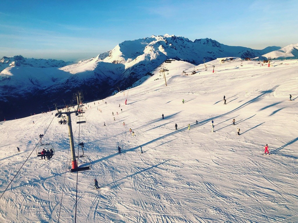 Chairlift crossing a golden-hour piste dotted with skiers