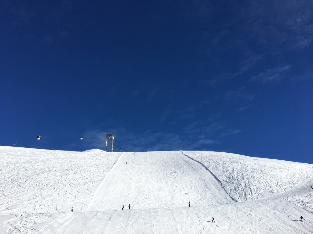Groomed piste rising toward the gondola line under a deep blue sky