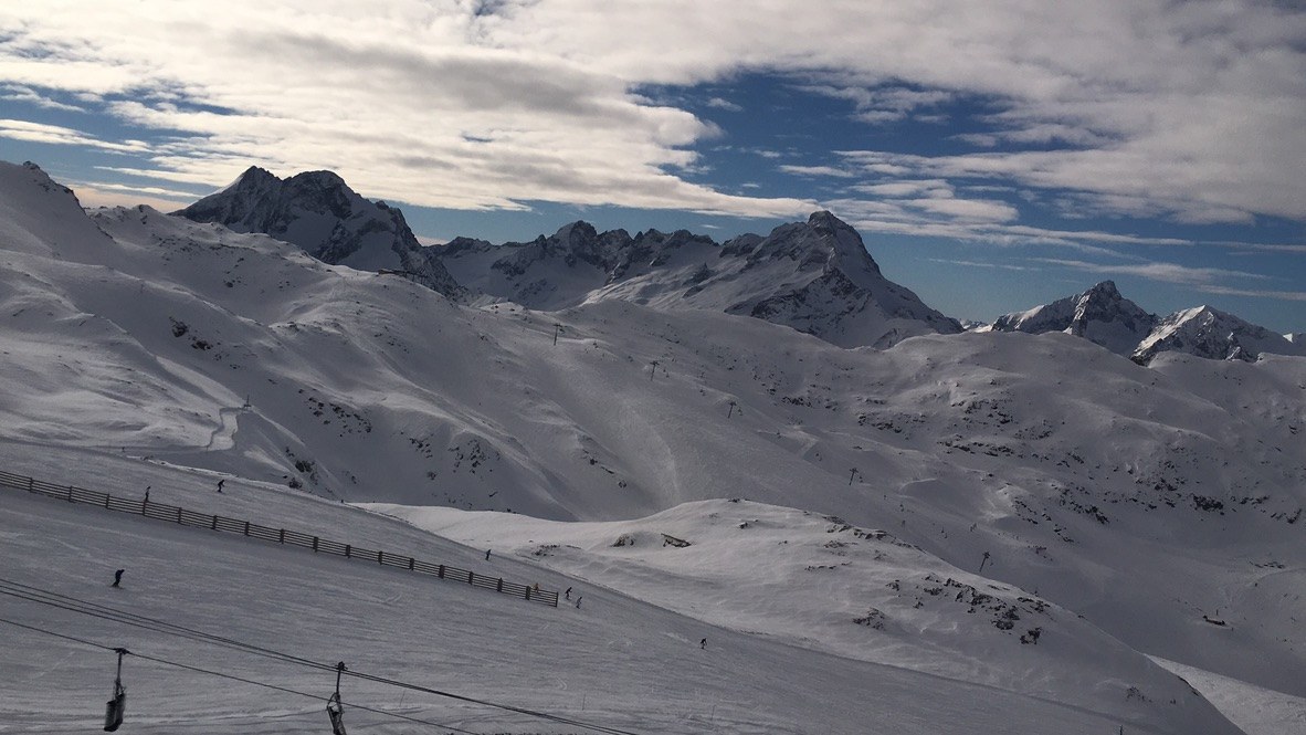 Skiers along the fence line below a jagged ridge